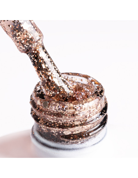 Pędzelek zanurzony w złotym brokatowym lakierze z drobinkami różnej wielkości