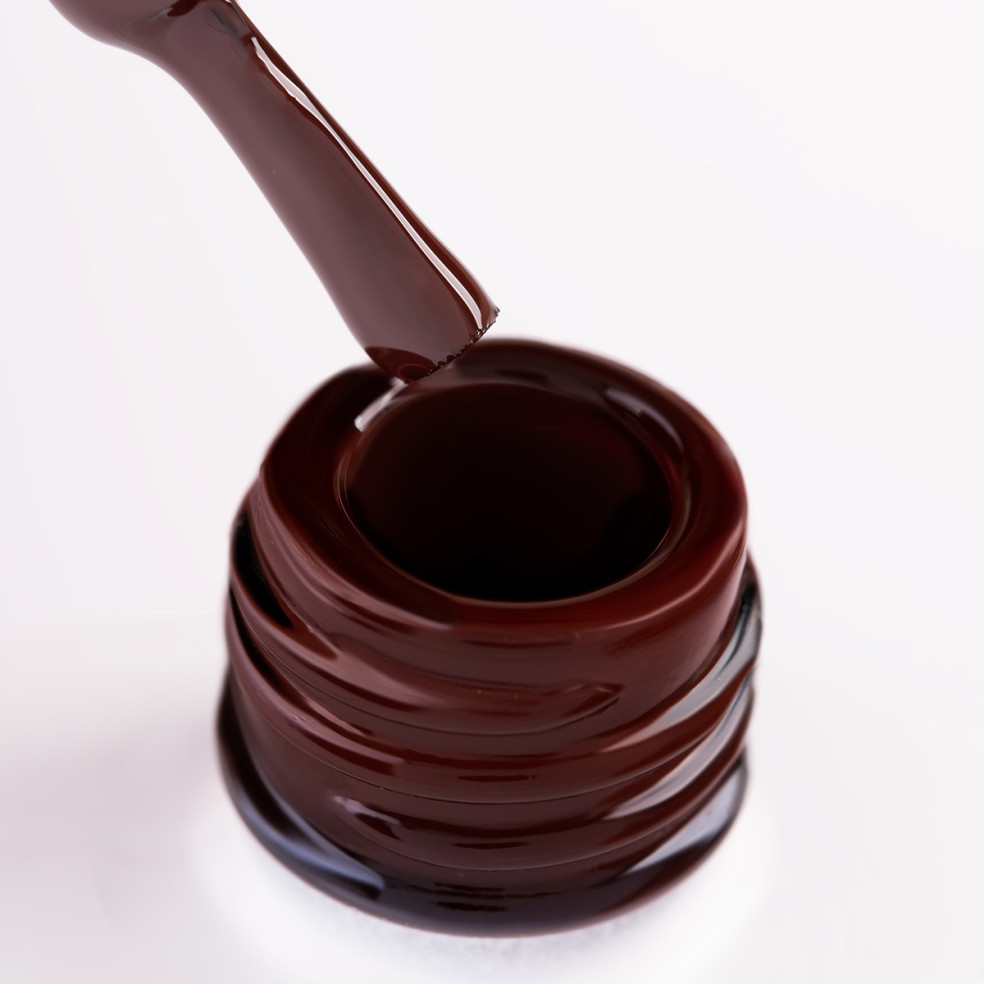 Szyjka butelki i oparty o nią pędzelek zanurzony w bordowym lakierze hybrydowym