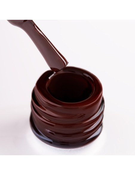 Szyjka butelki i oparty o nią pędzelek zanurzony w bordowym lakierze hybrydowym