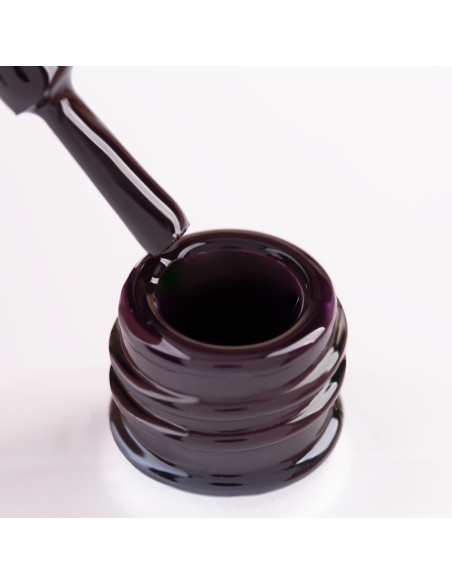 Szyjka butelki i oparty o nią pędzelek zanurzony w lakierze hybrydowym w kolorze ciemnym fioletowym