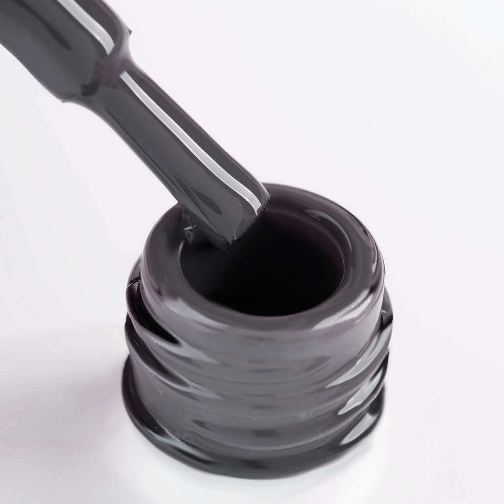 Szyjka butelki i oparty o nią pędzelek zanurzony w lakierze hybrydowym w kolorze ciemny szary