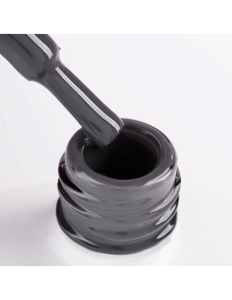 Szyjka butelki i oparty o nią pędzelek zanurzony w lakierze hybrydowym w kolorze ciemny szary