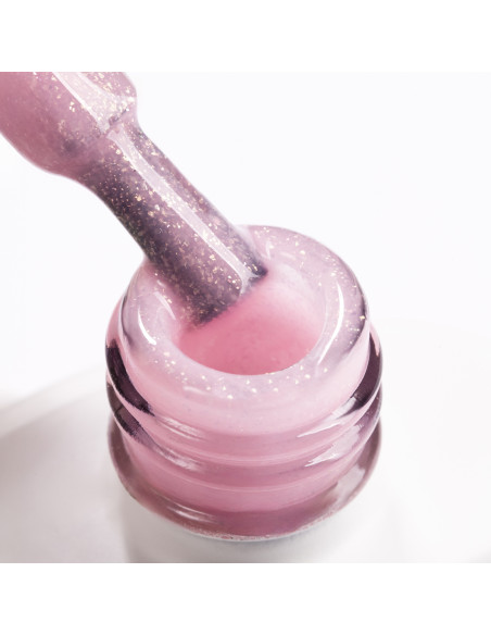 Pędzelek zanurzony w brzoskwiniowo różowym żelu do przedłużania paznokci z brokatowymi drobinkami