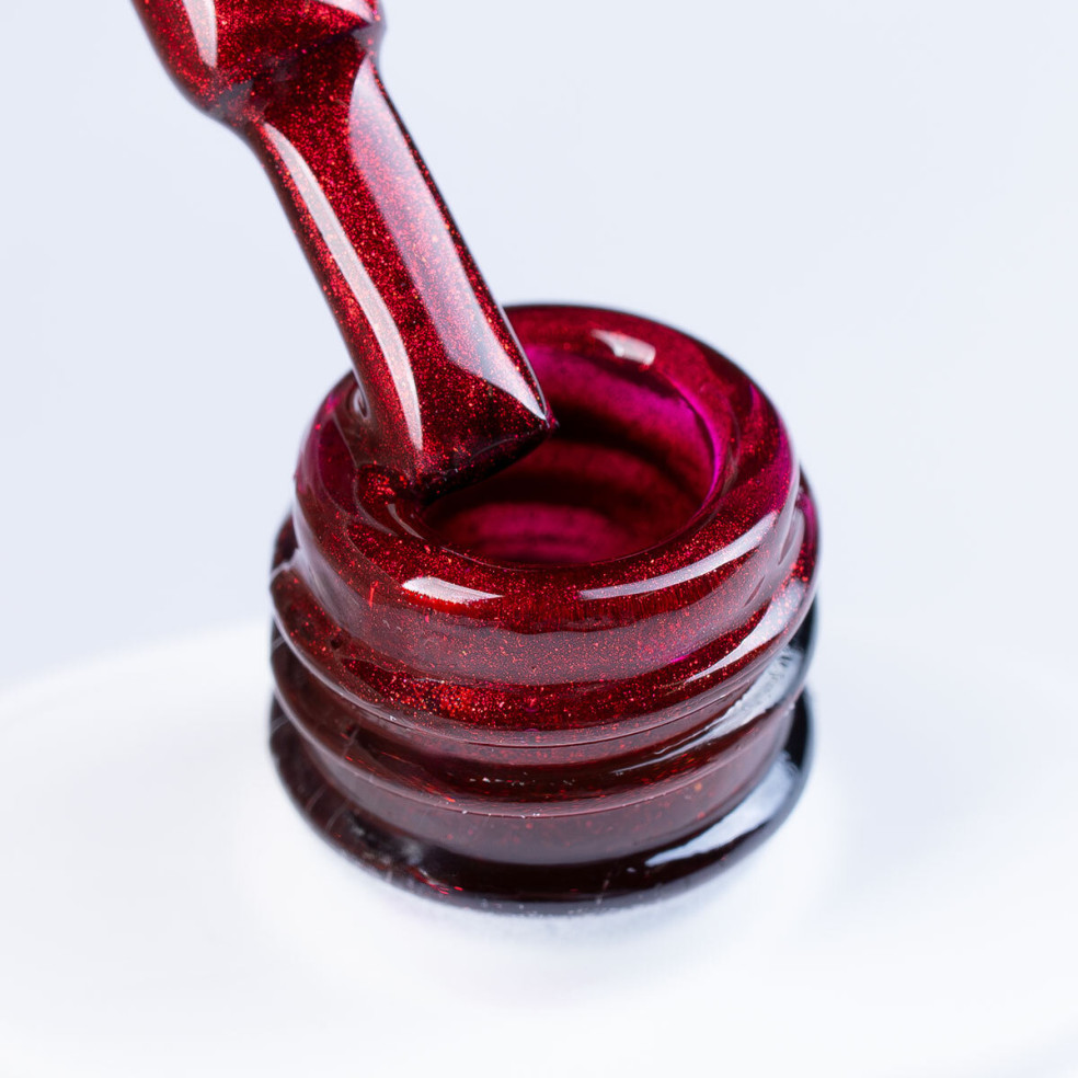 Szyjka butelki i pędzelek zanurzony w czerwonym brokatowym lakierze hybrydowym z efektem Cat Eye