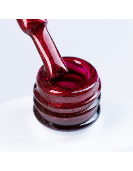 Szyjka butelki i pędzelek zanurzony w czerwonym brokatowym lakierze hybrydowym z efektem Cat Eye